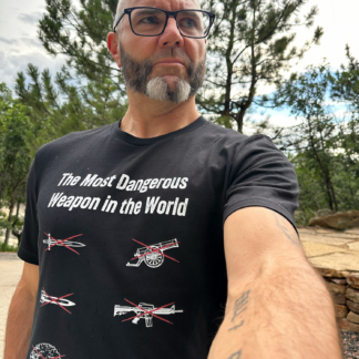 Male outside wearing a t-shirt that says, "Most Dangerous Weapon in the World". Illustrations crossed out include missile, sword, a-bomb, AR, cannon, the one not crossed out is a laptop computer.